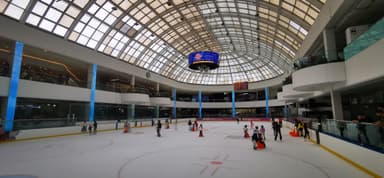 Une patinoire intérieure avec des enfants et des adultes en train de patiner sous un plafond en verre.