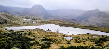 Un paysage de l'Azuay avec un lac et des collines sous un ciel nuageux.