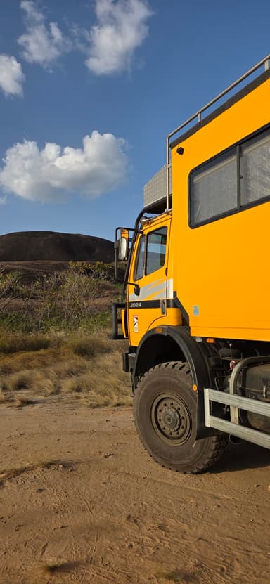 Un camion jaune sur un terrain désertique avec des collines en arrière-plan.