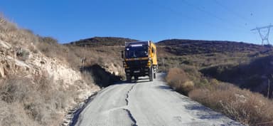 A yellow truck on a winding road surrounded by hills and clear blue sky.