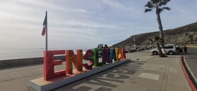 Colorful letters spelling 'ENSENADA' by the waterfront with palm trees.