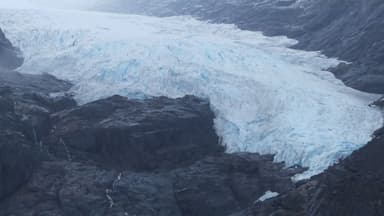 Un glacier bleu sur des rochers sombres sous un ciel brumeux.