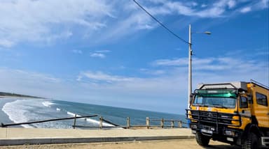 Un camion jaune sur une route côtière avec la mer en arrière-plan.