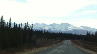 Une route menant vers des montagnes enneigées sous un ciel nuageux.