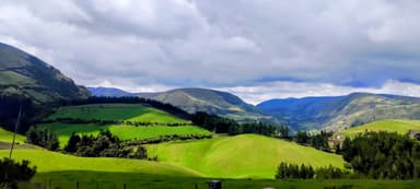 Un paysage verdoyant avec des collines et des montagnes sous un ciel nuageux.