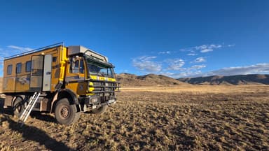 Un camion jaune dans un paysage montagneux ensoleillé.