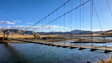 Un pont suspendu au-dessus d'une rivière avec des montagnes en arrière-plan.