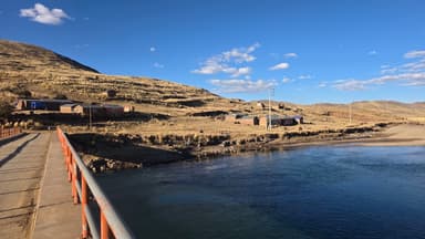Un paysage de collines et de maisons au bord d'une rivière sous un ciel bleu.
