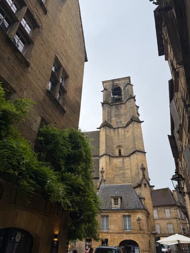 Une rue étroite avec une église en pierre sous un ciel nuageux.