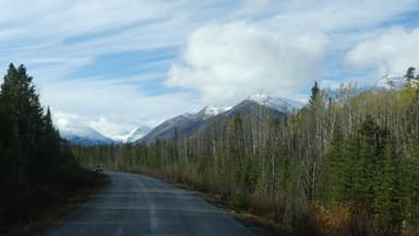 Une route bordée d'arbres avec des montagnes en arrière-plan sous un ciel nuageux.
