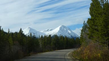 Une route sinueuse avec des montagnes enneigées en arrière-plan sous un ciel nuageux.