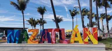 Un grand panneau coloré avec le nom de Mazatlán et des palmiers en arrière-plan.