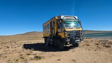 Un véhicule tout-terrain jaune sur un terrain désertique avec un lac en arrière-plan.