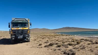 Un camion sur une plage près d'un lac sous un ciel bleu.