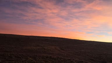 Un paysage de collines sous un ciel coloré au coucher du soleil.