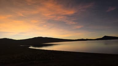 Un paysage de lac au coucher du soleil avec des montagnes en arrière-plan.