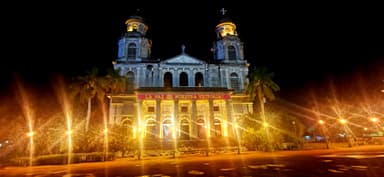 Une église illuminée la nuit avec des palmiers autour.