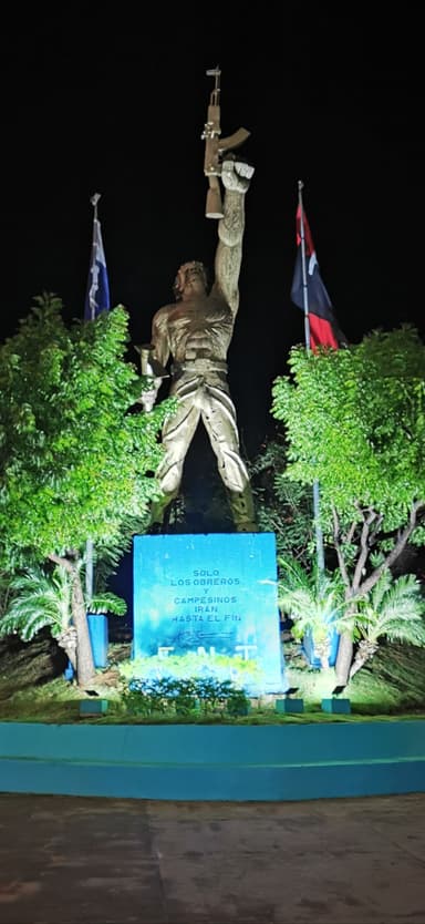Une statue illuminée la nuit avec des drapeaux autour.