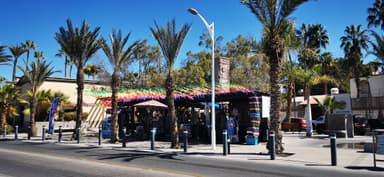 Un marché en plein air avec des palmiers et des décorations colorées sous un ciel bleu.