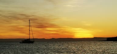 Un coucher de soleil sur l'eau avec un voilier.