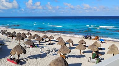 Plage de sable avec des parasols et des vagues bleues sous un ciel ensoleillé.