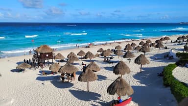 Plage de sable avec des parasols et des vagues turquoise.