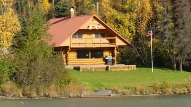 Une maison en bois au bord d'un lac avec des arbres colorés en arrière-plan.