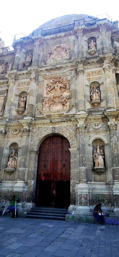 Une façade ornée d'une église à Oaxaca, avec des sculptures et une grande porte en bois.