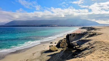 Une plage avec des falaises et des montagnes sous un ciel nuageux.