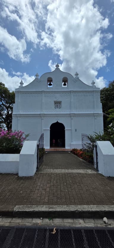 Une église blanche avec des fleurs colorées sous un ciel nuageux.