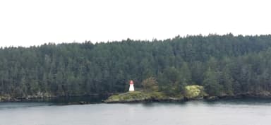 Un phare rouge et blanc sur une petite île entourée de forêts vertes.
