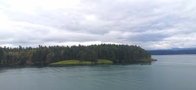 Une île verdoyante entourée d'eau calme sous un ciel nuageux.