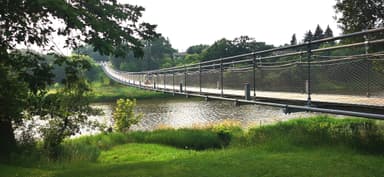 Un pont suspendu au-dessus d'une rivière entourée de verdure.