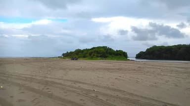 Une plage avec un îlot verdoyant au loin sous un ciel nuageux.