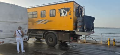 Un camion jaune sur un ferry au Venezuela avec un homme à côté.