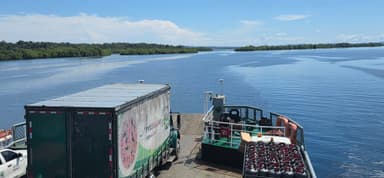 Un paysage de rivière avec un ferry et un camion sur l'eau.