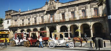 Des calèches blanches et rouges devant un bâtiment historique à Guadalajara.