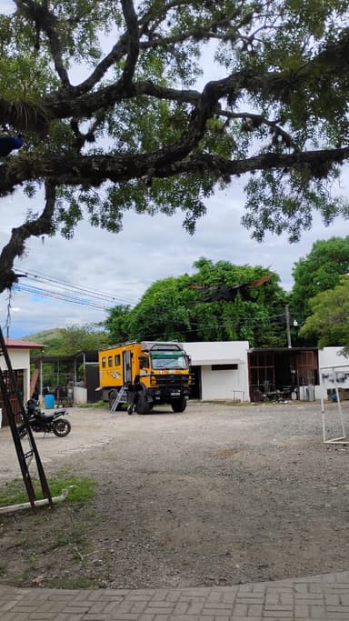 Un camion jaune garé sous un arbre dans une cour.