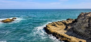 Une vue de la mer avec des rochers au premier plan et un ciel bleu.
