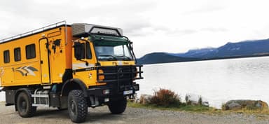 Un camion jaune stationné près d'un lac avec des montagnes en arrière-plan.