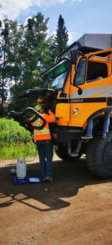 Un homme travaille sur un gros véhicule orange dans un environnement naturel.
