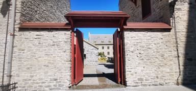 Une porte rouge encadrant un bâtiment en pierre sous un ciel bleu.
