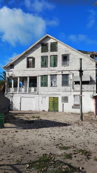 Une vieille maison blanche avec des volets verts sous un ciel bleu.
