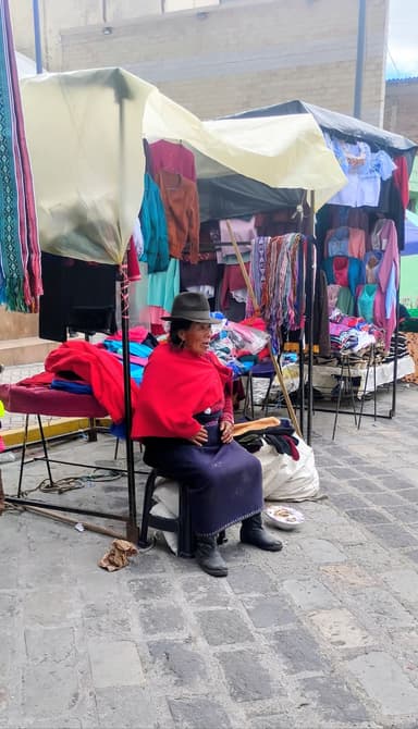 Une femme assise devant des étals colorés au marché.
