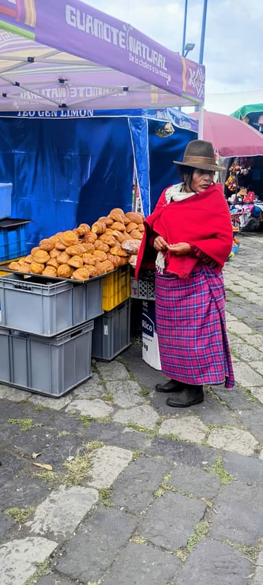 Une femme en poncho rouge vend des pains dans un marché.