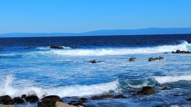 Une vue de l'océan avec des vagues et des rochers sous un ciel bleu.