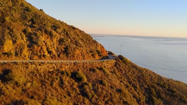 Une route sinueuse sur une colline surplombant l'océan au coucher du soleil.