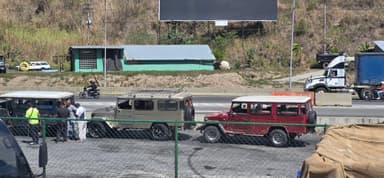 Des véhicules stationnés près d'une route à Miranda, Venezuela, sous un ciel ensoleillé.