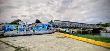 Un pont métallique avec des graffitis colorés au bord de l'eau.