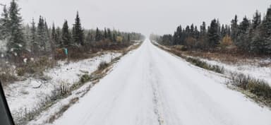 A snowy road surrounded by trees in a remote area.
